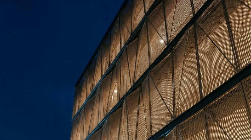 Perforated-metal screen facade on a steel sub-frame glowing at dusk — architectural visualisation