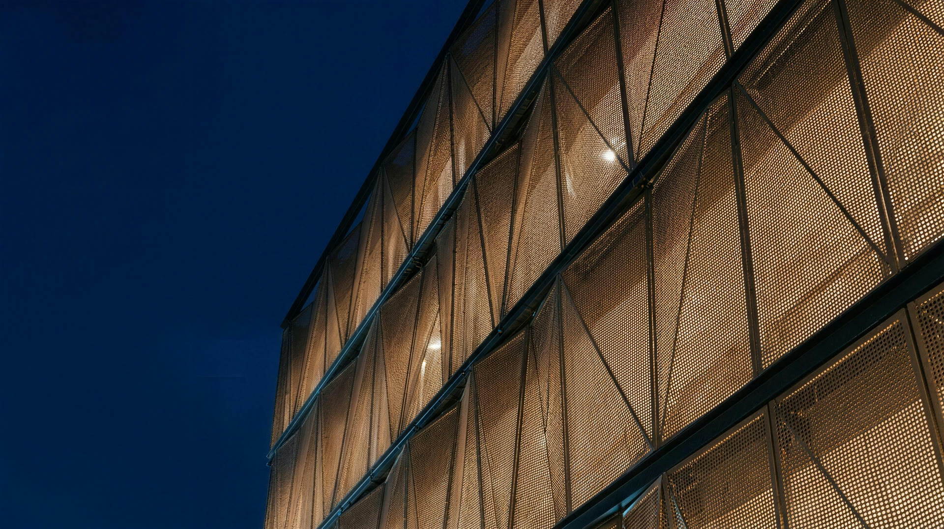 Perforated-metal screen facade on a steel sub-frame glowing at dusk — architectural visualisation