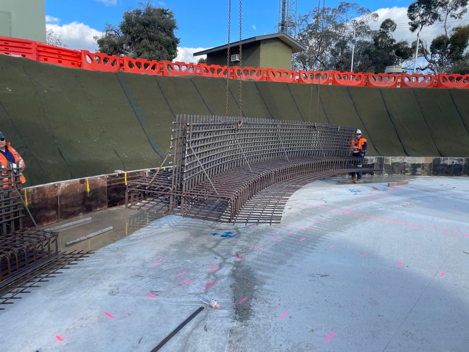 Curved reinforcement cage slung from a mobile crane over a circular tank base — Metric cage-lift design, Gawler East SA