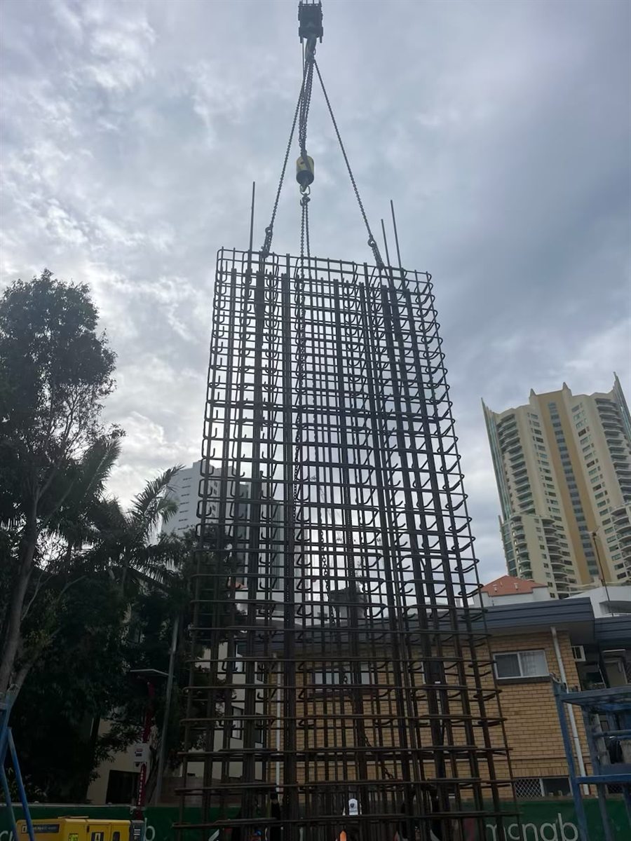 Tall diaphragm-wall reinforcement cage lifted vertically by a crawler crane against the Gold Coast skyline